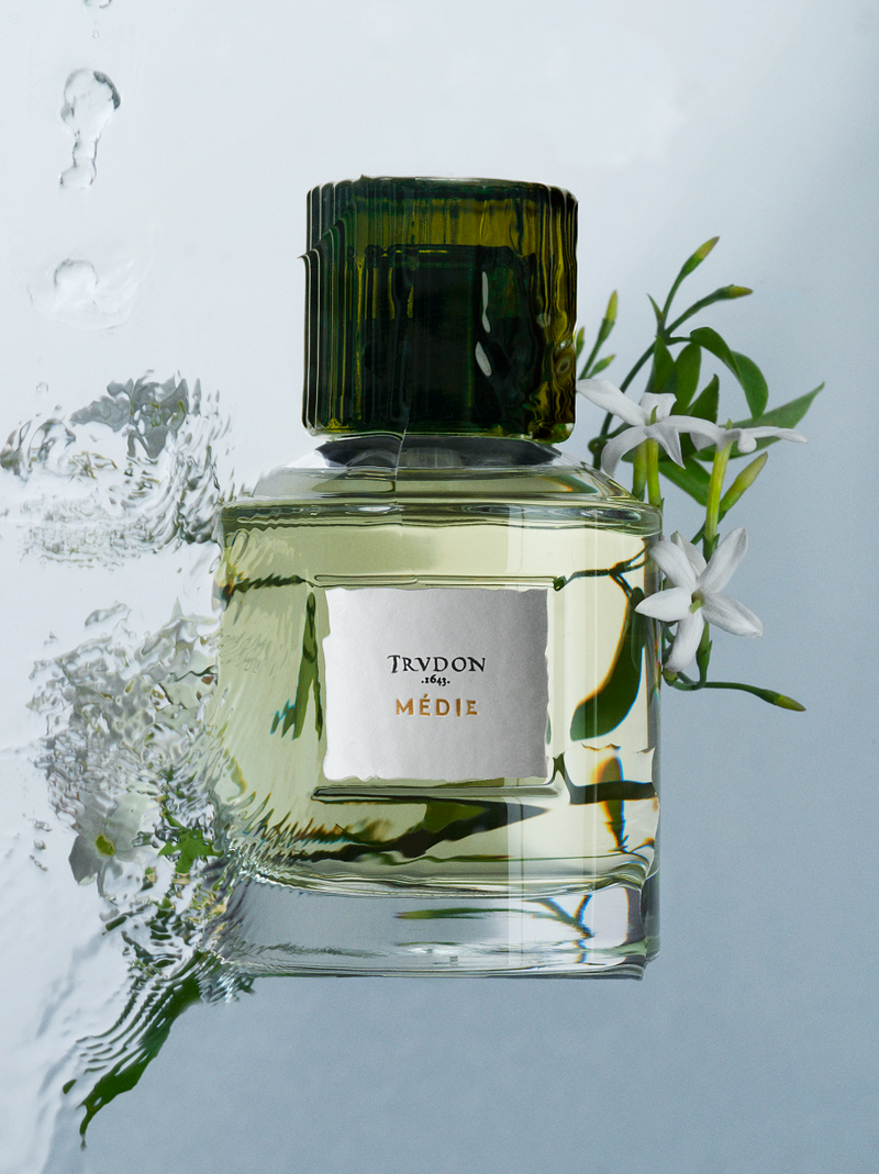 Cire Trudon | Medie Perfume | Scent Lounge | Lifestyle Image of Perfume Bottle, Blue Background with Water & Flowers
